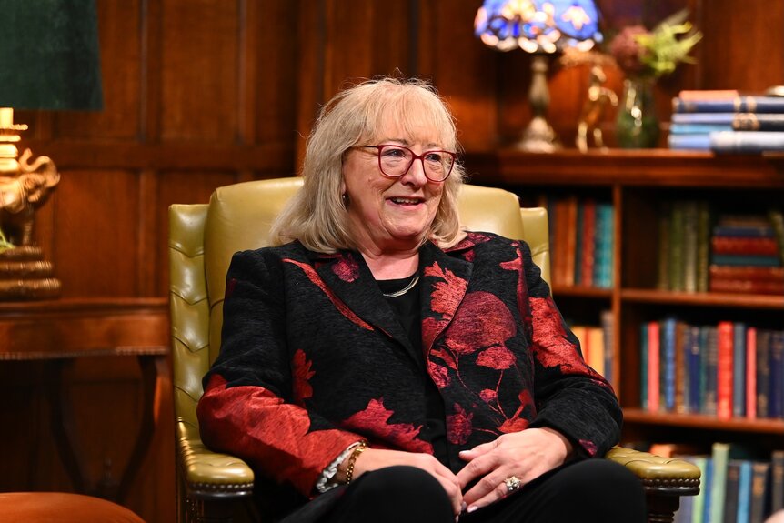 Donna Kelce wears a red patterned blazer and sits in an armchair on The Traitors Episode 401.