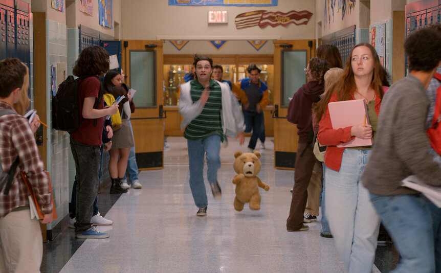 John (Max Burkholder) and Ted (Seth MacFarlane) running down a school hallway in Ted Season 2.