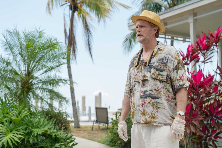 Kincaid looking while outside surrounded by flowers and palm trees in M.I.A. Season 1 Episode 2.